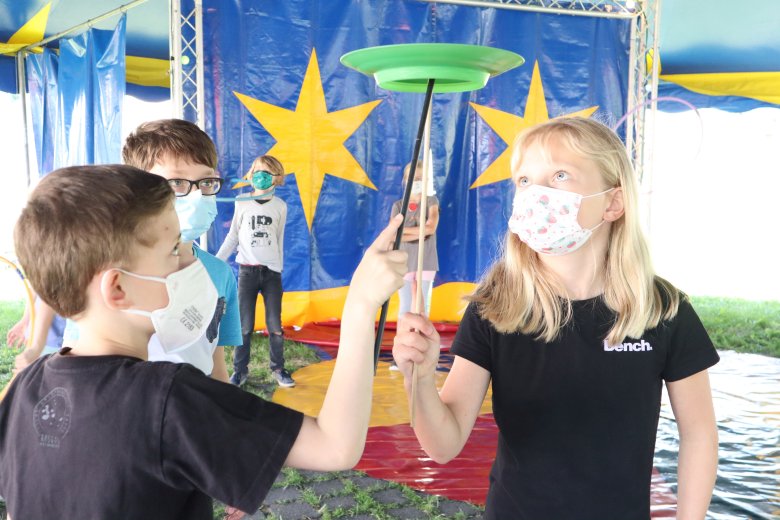 Auf dem Bild sieht man mehrere Kinder die probieren einen Zirkusteller auf einem Holzstarb zu Balenzieren 