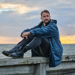 Musiker Florian Künstler sitzt auf einer Mauer. Im Hintergrund ist Meer zu sehen