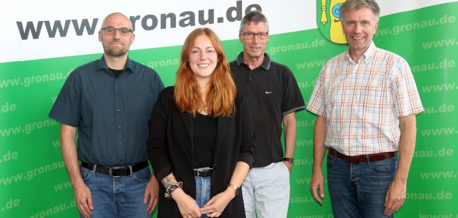 Vertretungen der Caritas und der Verwaltung der Stadt Gronau vor einer grünen Messewand.