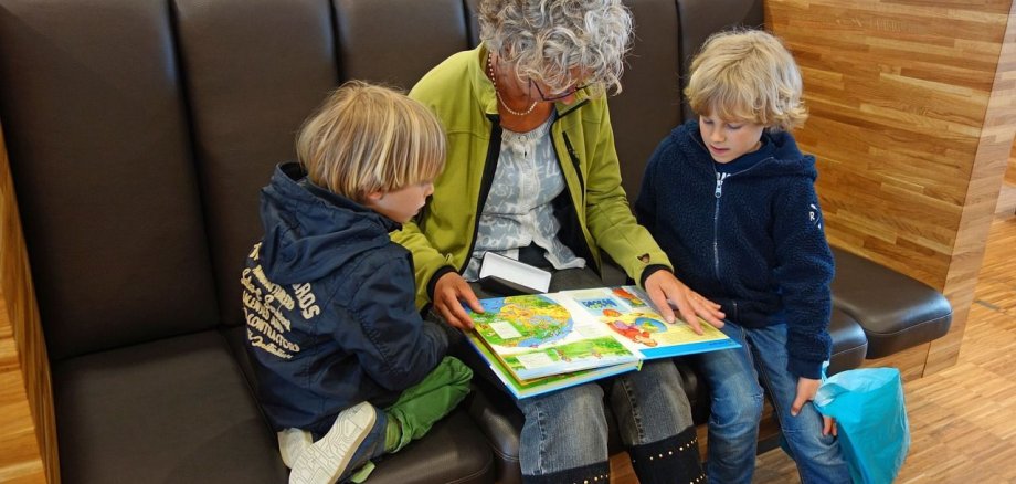 Eine ältere Frau liest zwei kleinen Kindern ein Buch vor