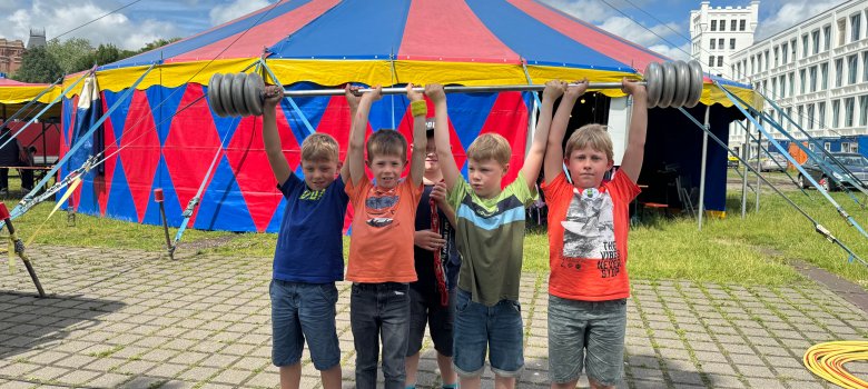 Kinder, die an den Ferienspielen 2024 im Zirkus Merlin teilnehmen, stehen vor einem Zirkuszelt